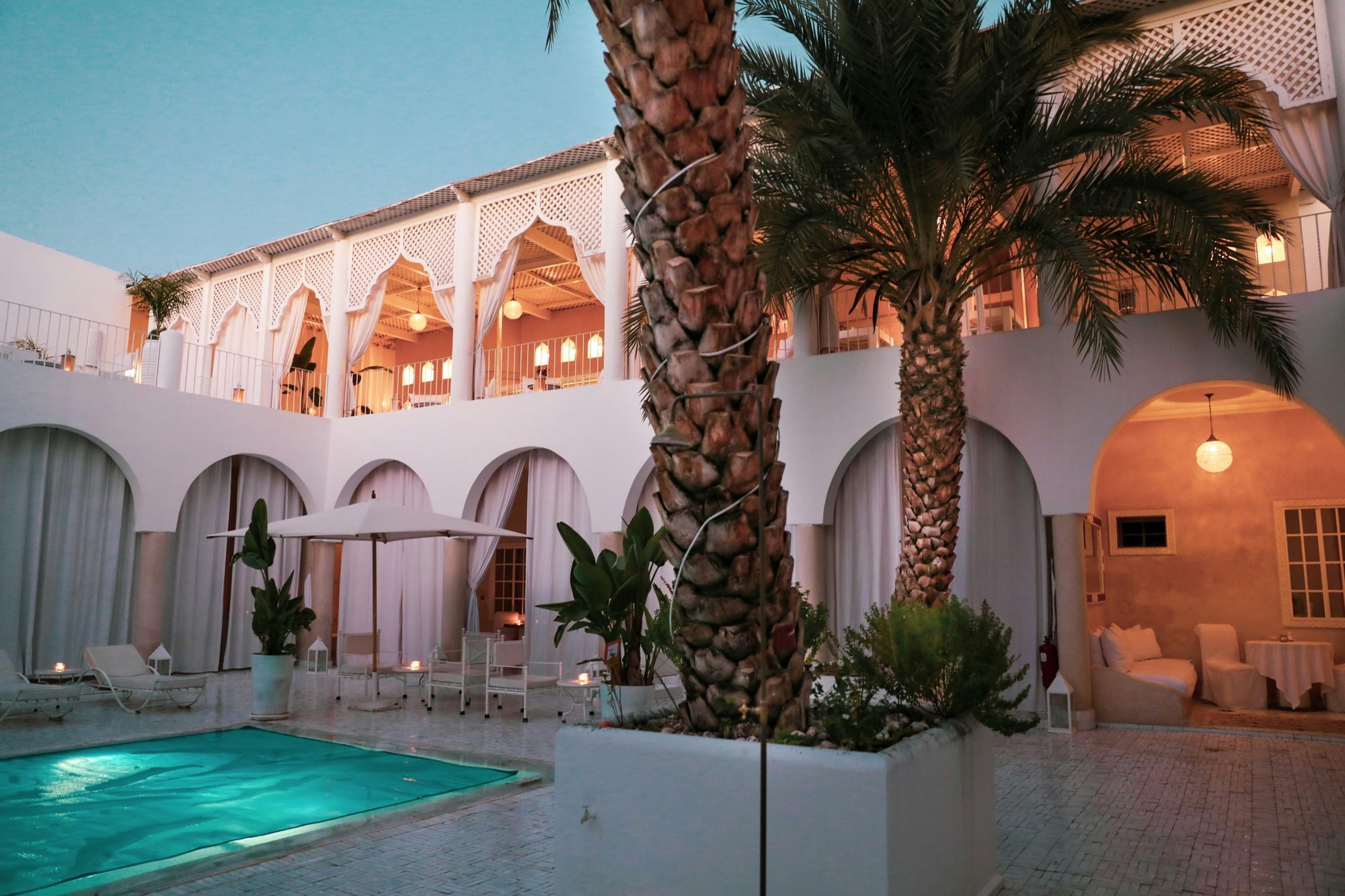 A riad pool and arcaded terraces lit at dusk